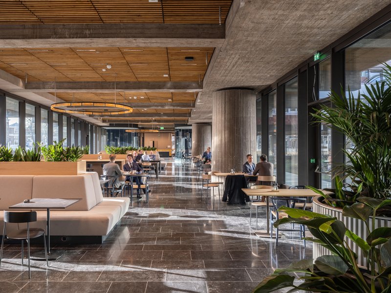 Cafe space with dark stone flooring, timber ceiling, cylindrical concrete columns and seated occupants