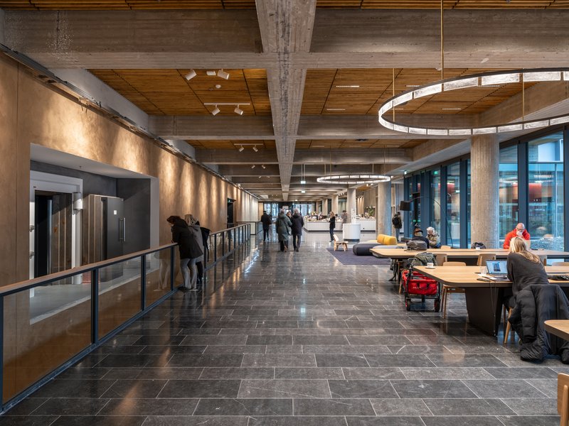Circulation corridor with dark stone floor, timber ceiling panels, circular pendant lights and people gathering