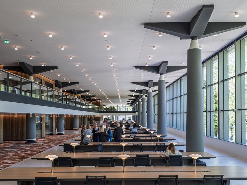Double-height reading room with long study tables, cylindrical columns, and angular black ceiling baffles