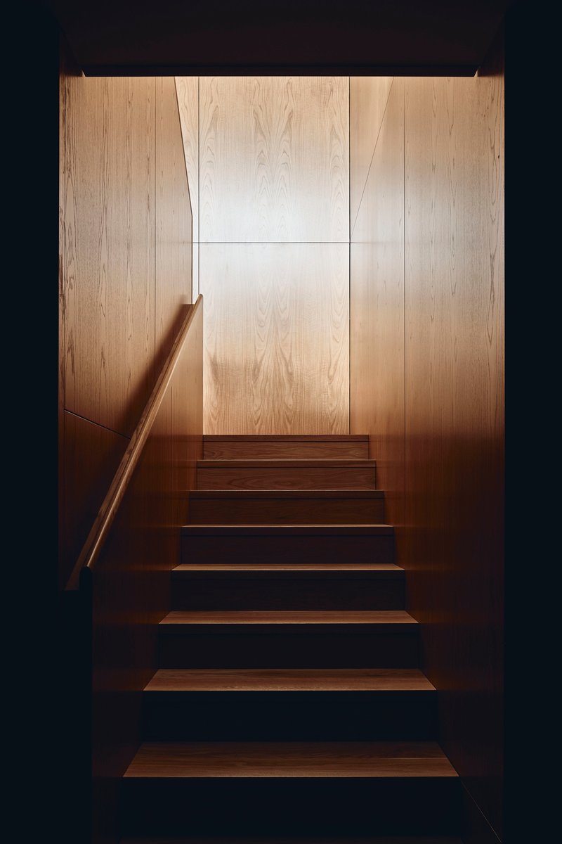 Timber staircase with cantilevered treads and blonde wood wall panels illuminated from above