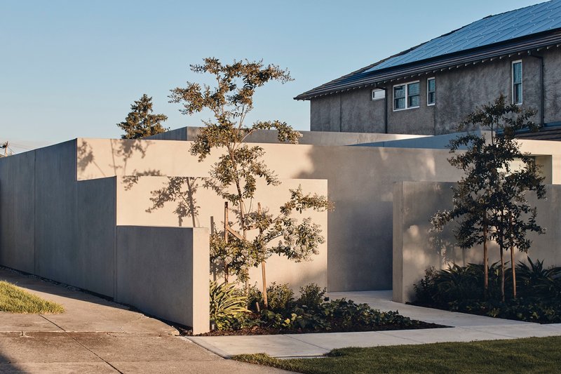 Stepped concrete entry wall with planted trees casting shadows in afternoon light