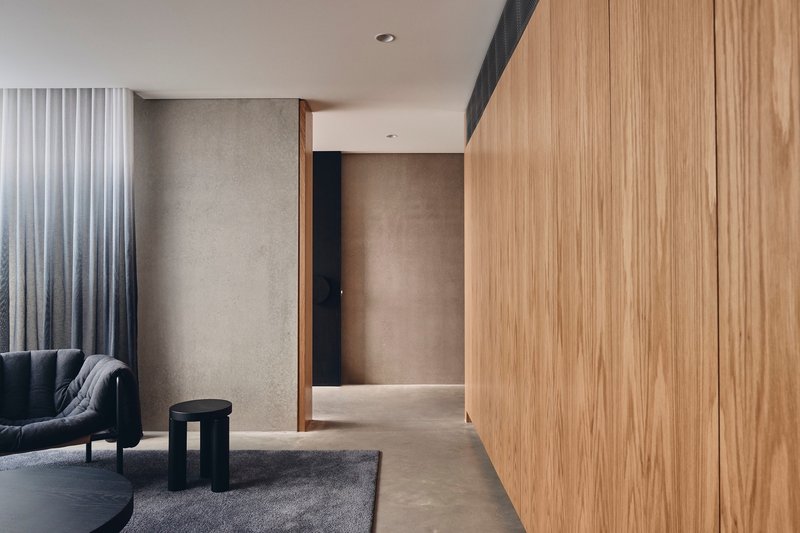 Timber-clad corridor with concrete walls and grey curtains beside a seating area