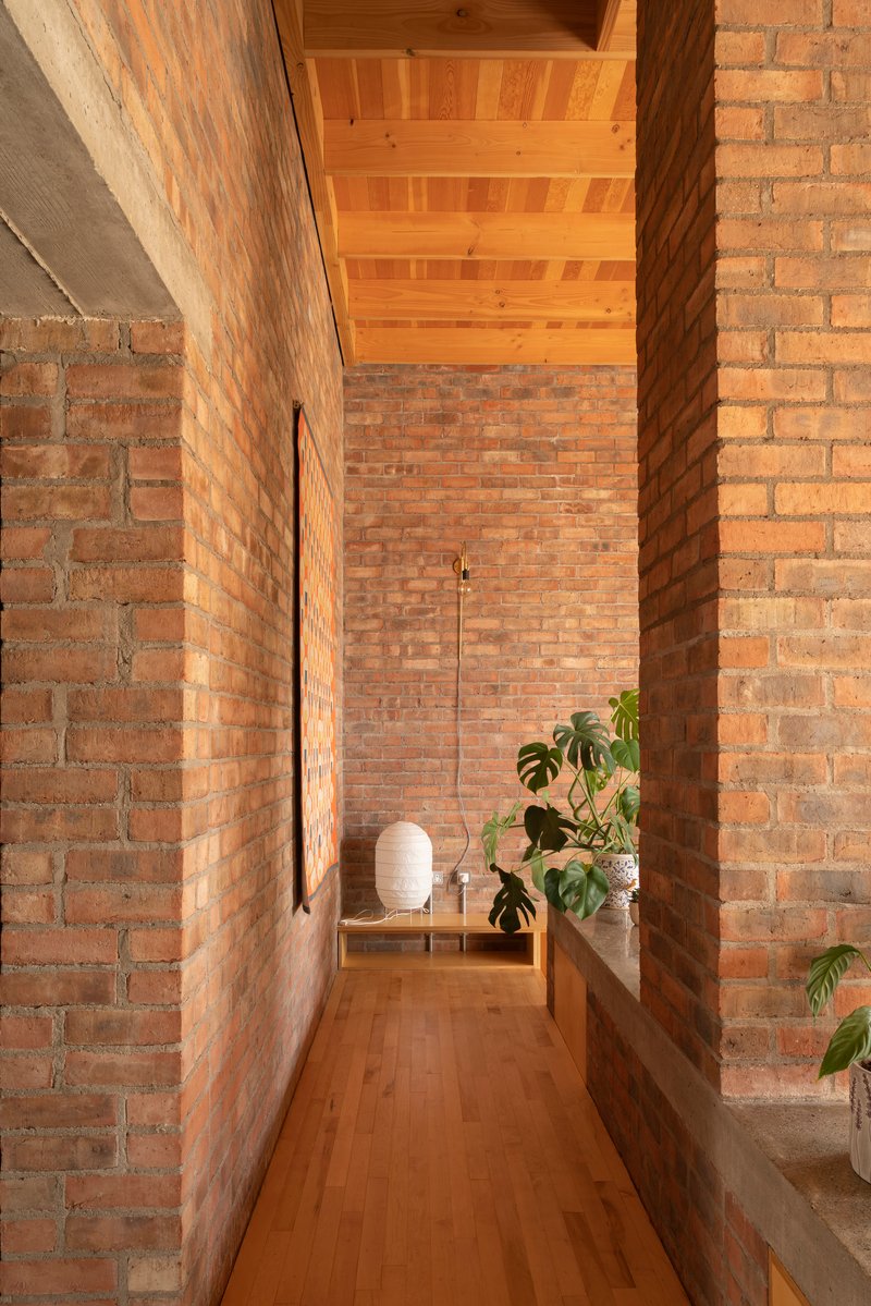 Narrow corridor with exposed brick walls, timber ceiling beams and potted monstera plants on a concrete ledge