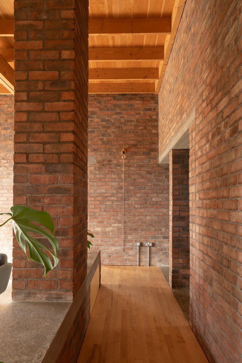 Interior passage framed by brick piers with a suspended pendant light and timber flooring in afternoon light