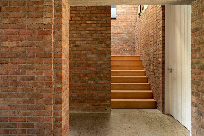 Timber staircase rising between exposed brick walls with a white ribbed door and polished concrete floor