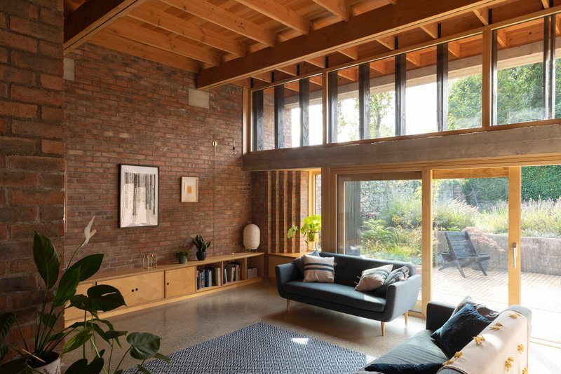 Double-height living space with exposed timber beams, brick walls and clerestory windows overlooking a terrace