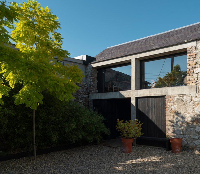 Slate-roofed extension with concrete frame and timber cladding beside a stone wall and potted trees