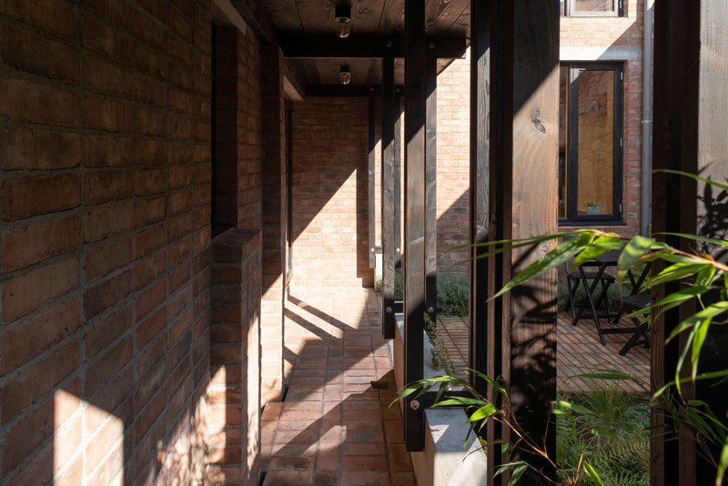 Glazed corridor with steel frame casting sharp shadows on brick walls and paved floor