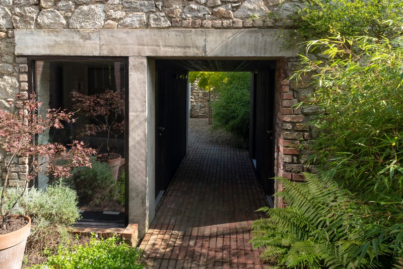 Concrete portal framing a brick-paved passage through a stone wall with planted beds and ferns