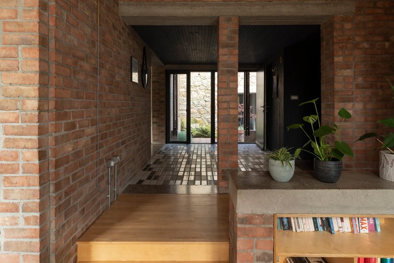 Entry corridor with brick walls and dark timber ceiling leading to glazed door and stone wall