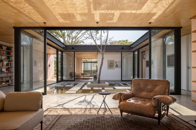 Living room with leather chairs looking through glazed walls to courtyard tree and stepped pavers