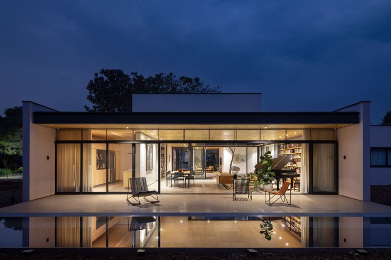 Fully glazed facade opening to terrace and reflecting pool with interior furniture visible at twilight