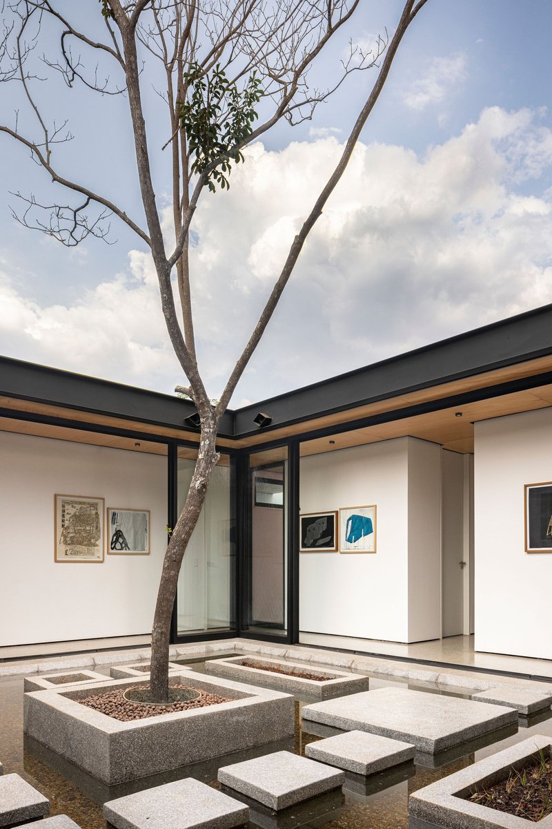 Courtyard corner showing concrete planter with tree, stepping stones, and gallery walls under cloudy sky