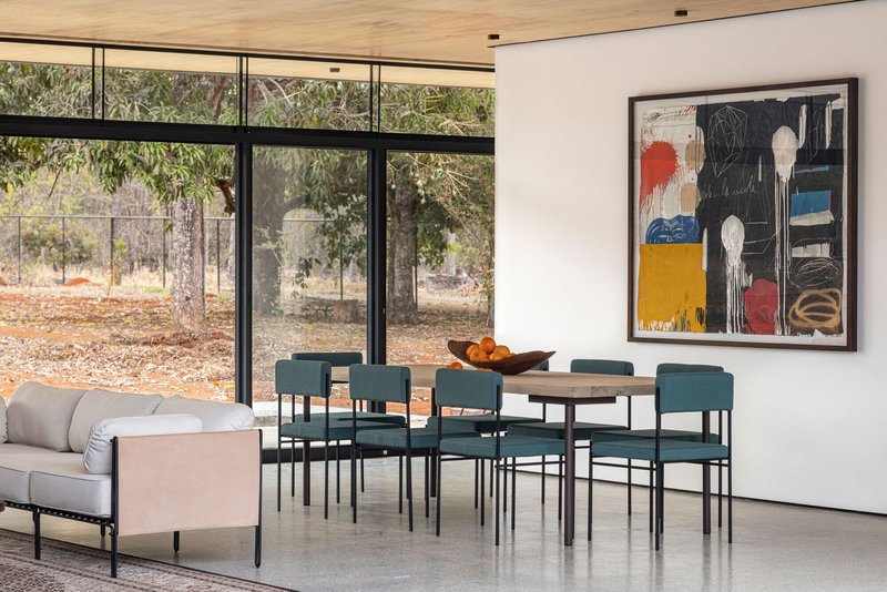 Living and dining space with steel-framed windows overlooking a dry landscape of trees and gravel