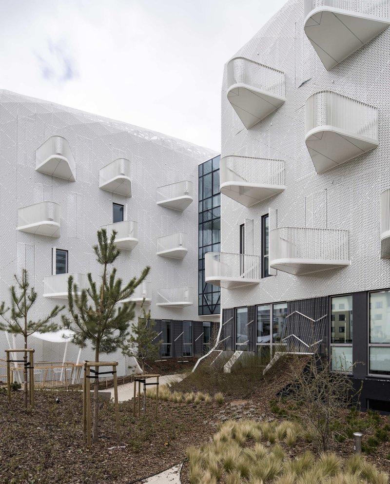 Courtyard showing triangular balconies on perforated white walls with native grasses and wooden benches in gravel