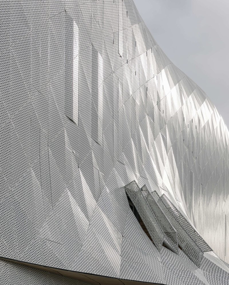 Close view of the perforated metal facade casting diagonal shadows across its textured surface