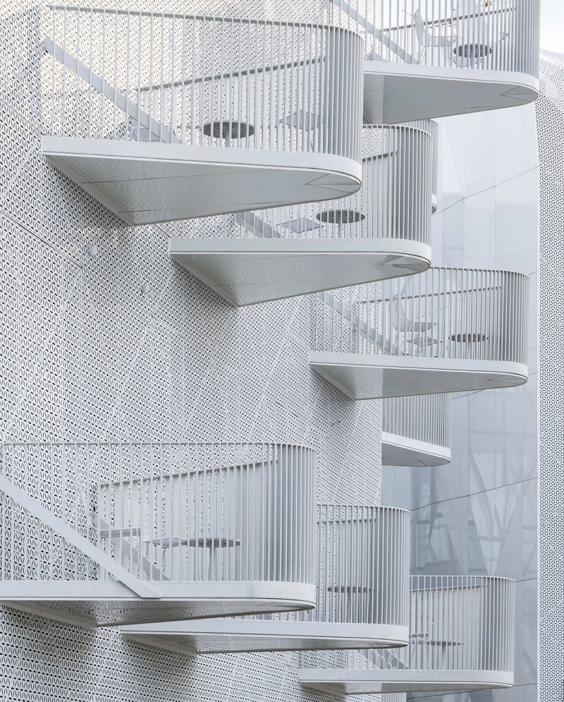 White spiral staircase with perforated metal walls and curved treads in diffuse light