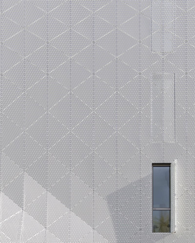 White perforated metal facade with a single narrow vertical window opening