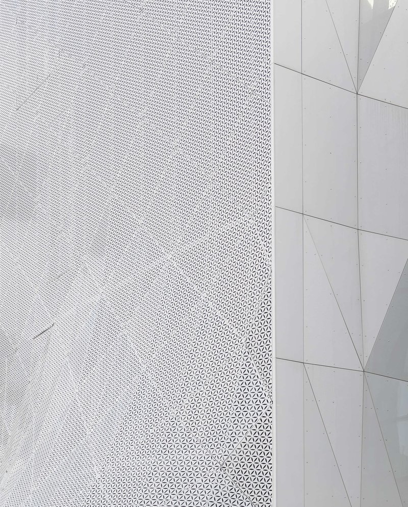 Corner detail where perforated white metal cladding meets smooth flat paneling