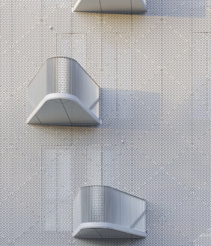 Overhead view of curved metal canopies projecting from a perforated white facade