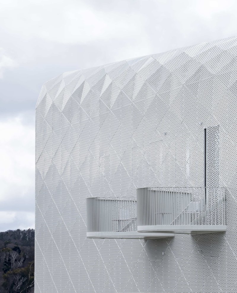 Side view of a curved perforated metal volume with canopy openings under cloudy skies