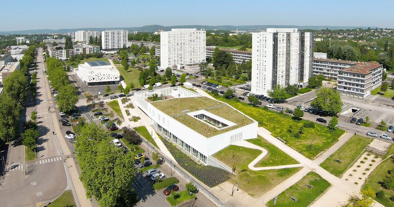 Aerial view showing the rectangular building with green roof courtyard surrounded by residential towers and tree-lined streets