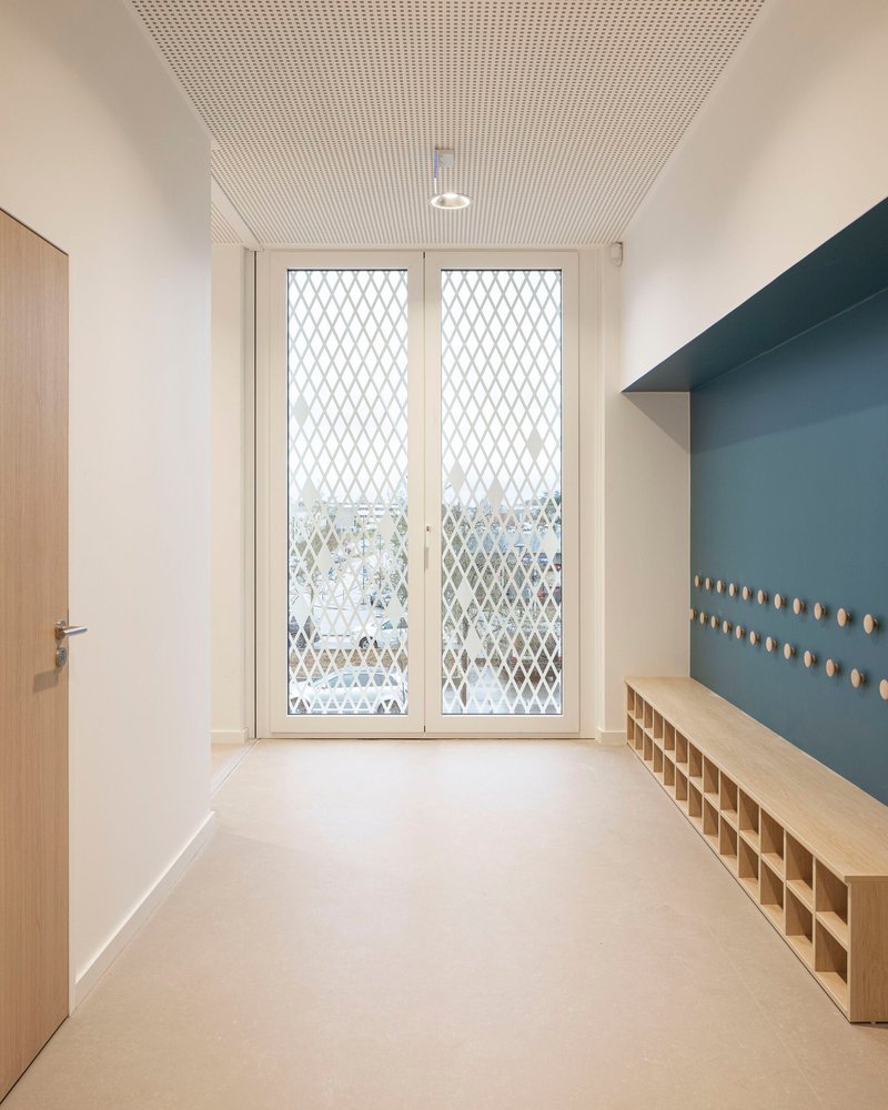 Entry corridor with plywood bench, blue pegboard wall and diamond mesh glazed doors