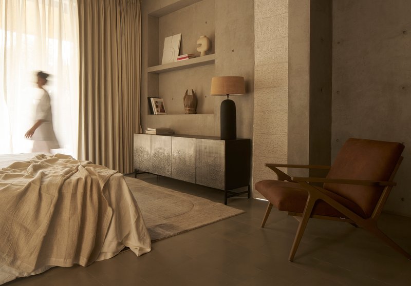 Bedroom with floating shelves and person passing through soft natural light from sheer curtains
