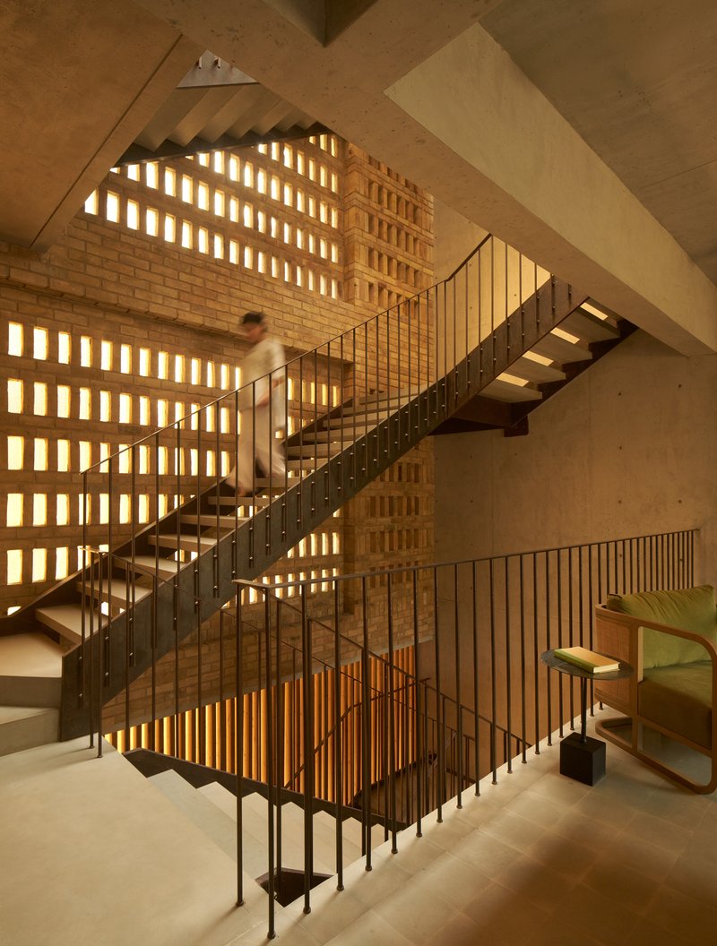 Central stairwell with steel and timber stair illuminated by backlit perforated brick walls