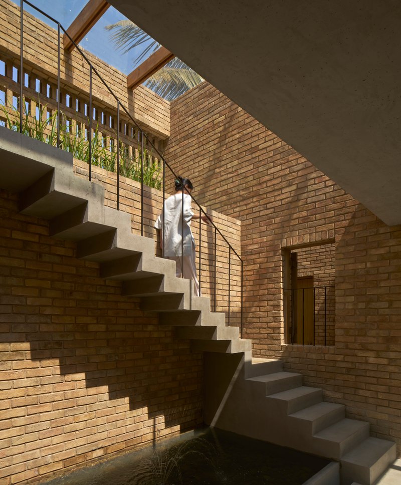 Concrete staircase rising through a brick courtyard with clerestory openings and a figure ascending