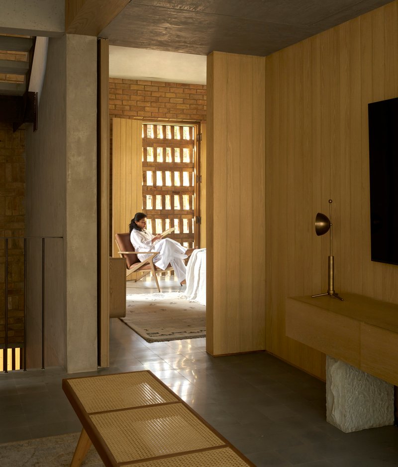 View through timber-lined hallway toward seating alcove with gridded brick light screen