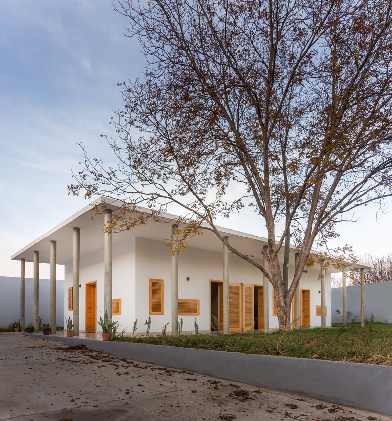 Gabled white volume with wood shutters and columned porch beneath a bare tree at dusk