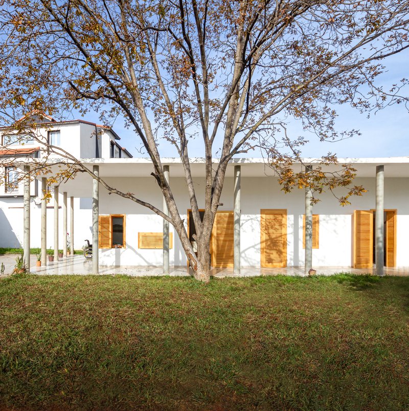 White stucco facade with timber shutters and columned porch beneath a deciduous tree in autumn foliage