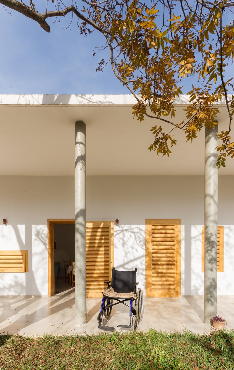 Covered porch with white columns and timber louvered doors casting dappled shadows with wheelchair present
