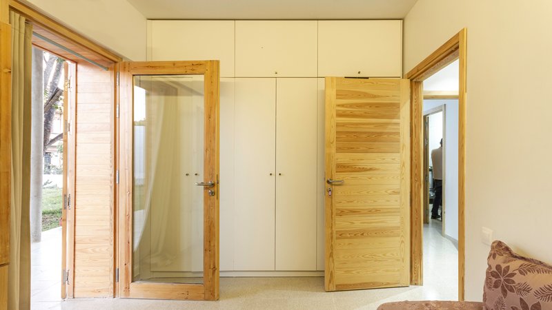 Interior bedroom corner with timber-framed louvered doors and white built-in wardrobes flanking timber panel door