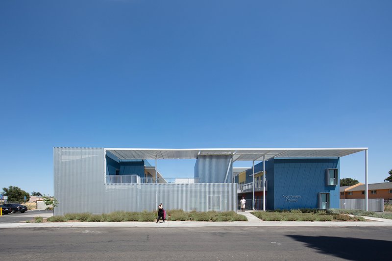 Street view of the corrugated metal facade with upper level canopy and a pedestrian walking past
