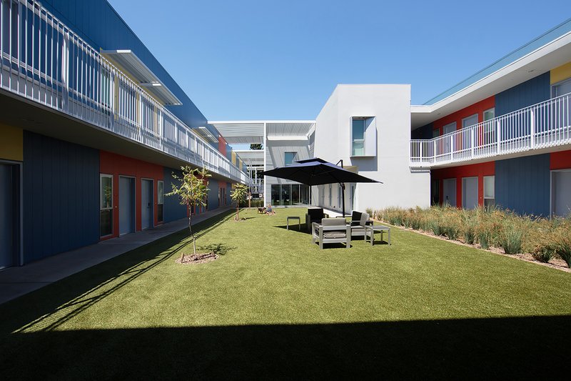 Courtyard lawn framed by residential units with blue and orange panel facades and upper-level walkways