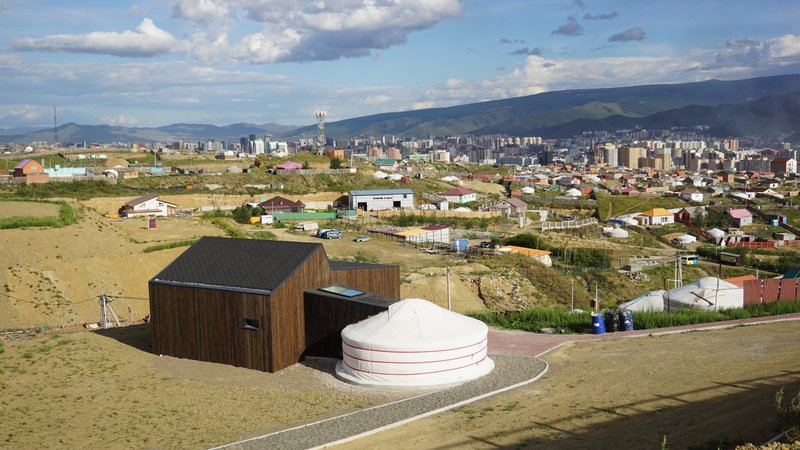 Elevated perspective of the timber box and white yurt set against distant mountains and suburban sprawl