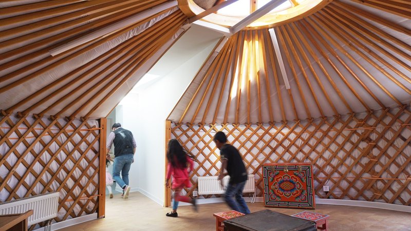 Interior of the yurt showing radial timber ceiling ribs and lattice walls with children in motion