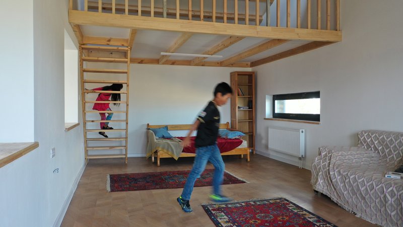 Bedroom with exposed timber joists and ladder access to a loft as a child walks past