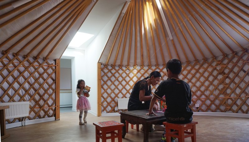 Interior of the yurt showing radial timber roof beams and lattice walls with a family gathered inside