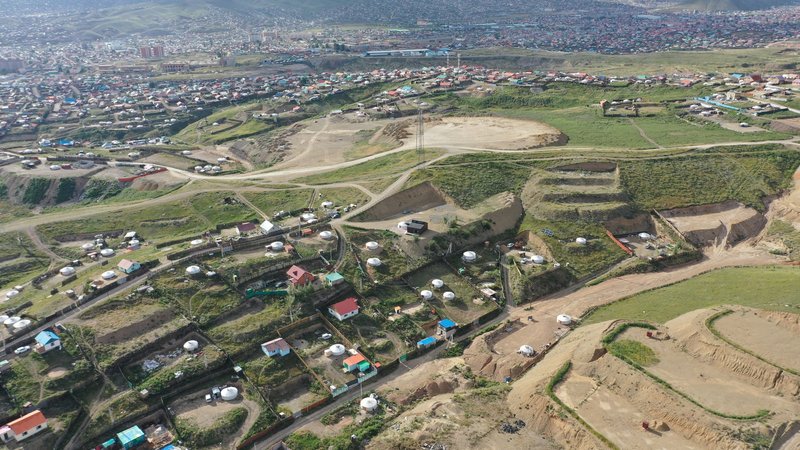 Aerial view of a residential settlement with dirt roads and cultivated plots along a hillside