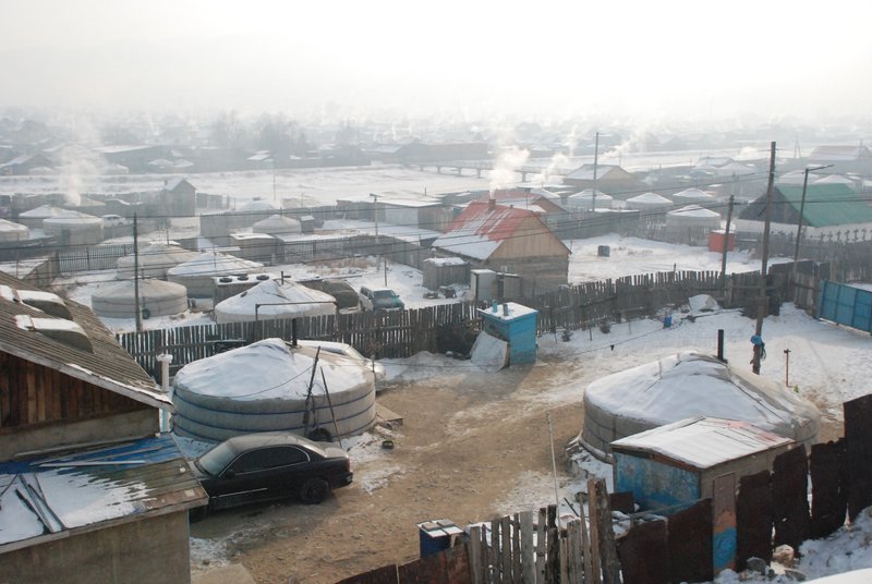 Winter view of multiple circular yurt dwellings along a snowy street with rising smoke