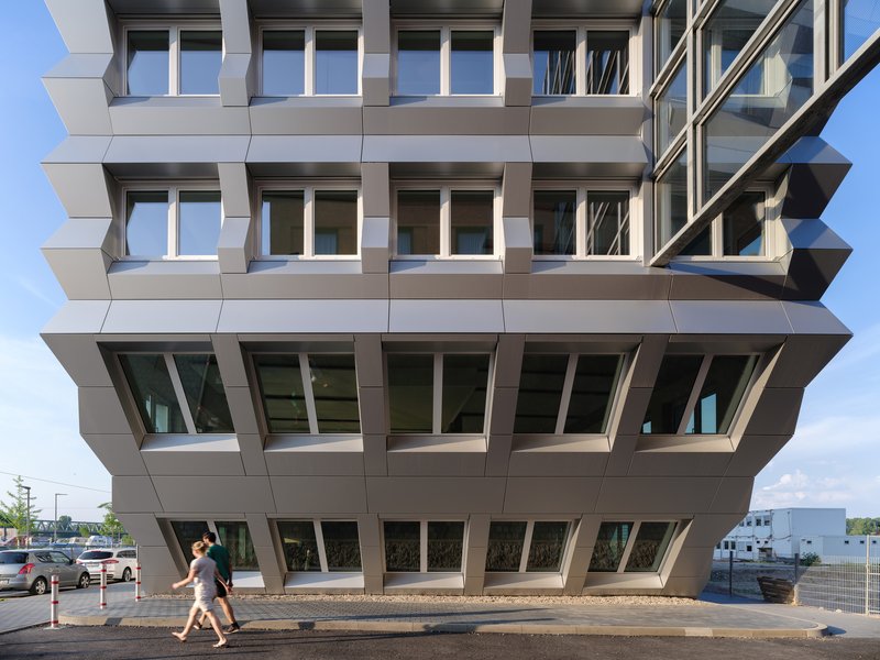 Close view of the cantilevered ground floor with angled window frames and pedestrians walking beneath