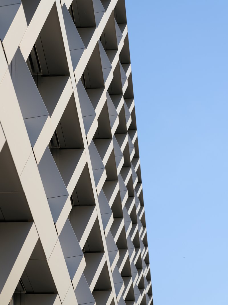 Angled view of the crisscrossing white facade fins creating a diamond pattern against clear blue sky