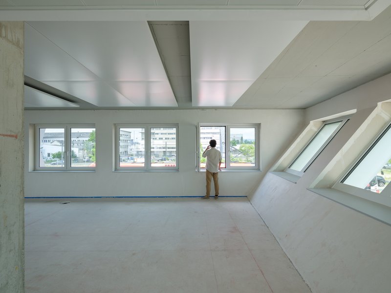 Interior with angled skylight and windows where a person stands gazing at the urban view