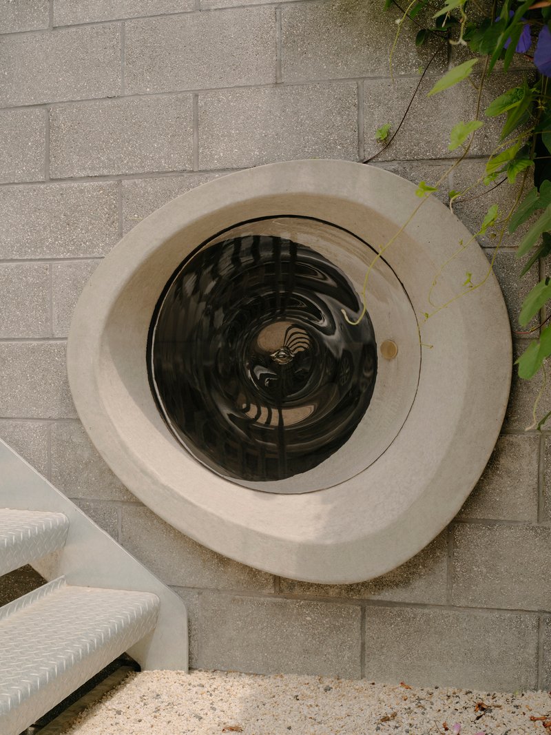 Overhead view of a circular skylight set into a concrete frame on a paved terrace with foliage