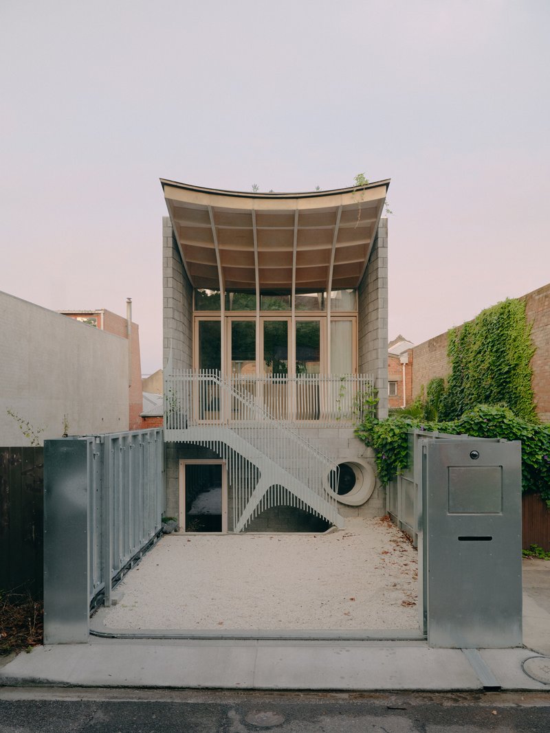Street view of the curved timber roof and vertical slat facade with circular window under overcast sky