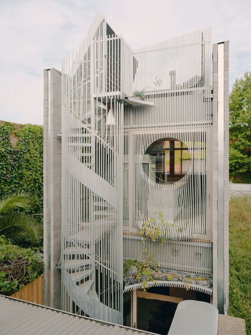 Facade detail showing vertical metal slats wrapping the curved form with circular window and exterior stair