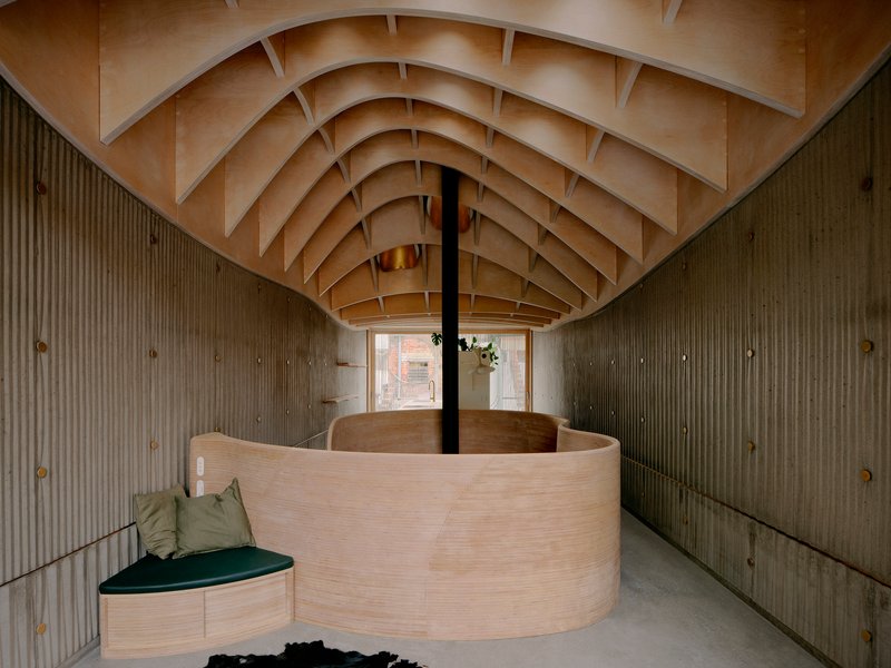 Interior view of curved plywood partition wall beneath exposed laminated timber vault ceiling with brass pendant